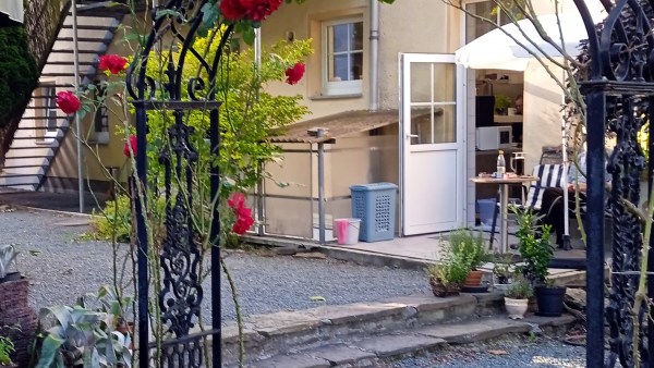 Schwarzer Rosenbogen mit roten und weißen Rosen auf Schotterboden vor einem Haus